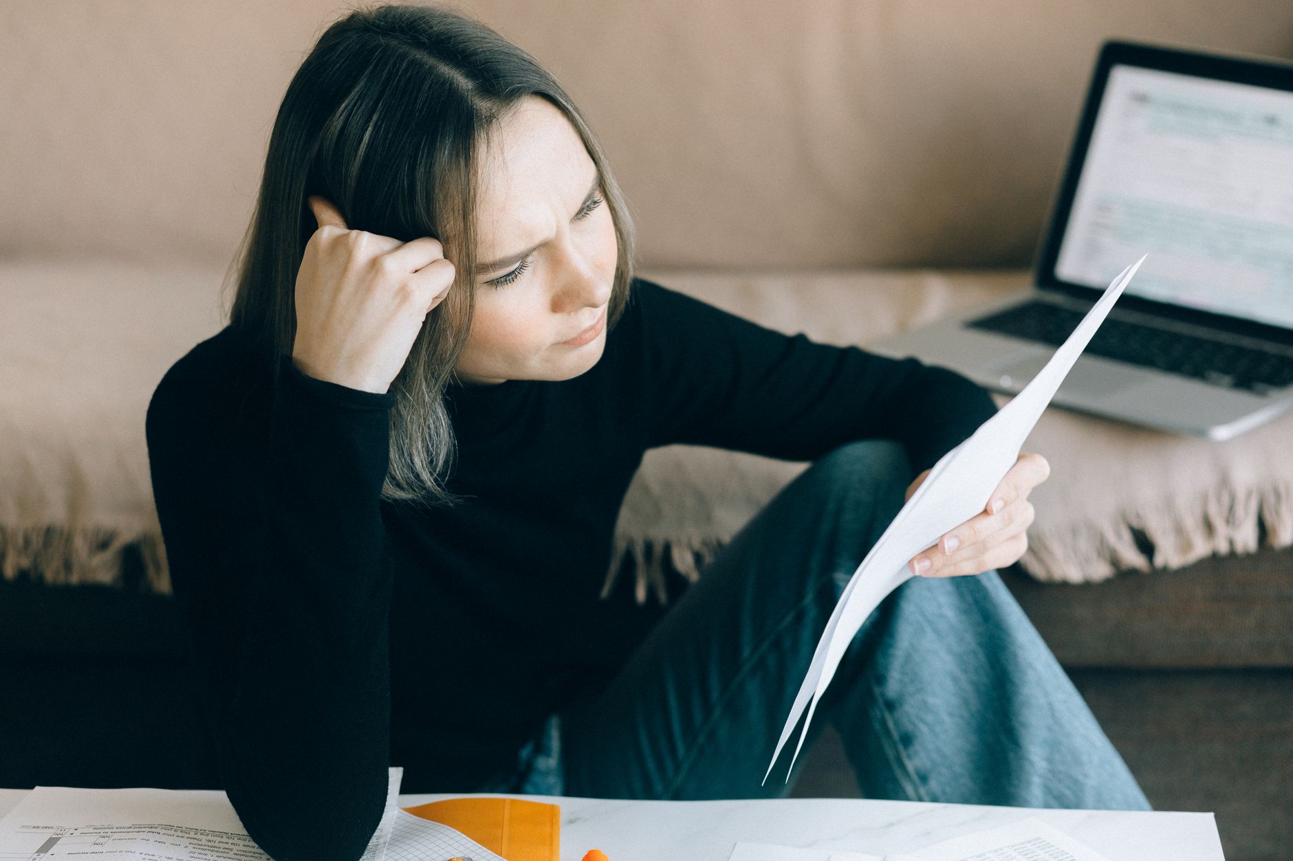A person sits at a kitchen table reviewing a credit report on a laptop, with paperwork nearby.