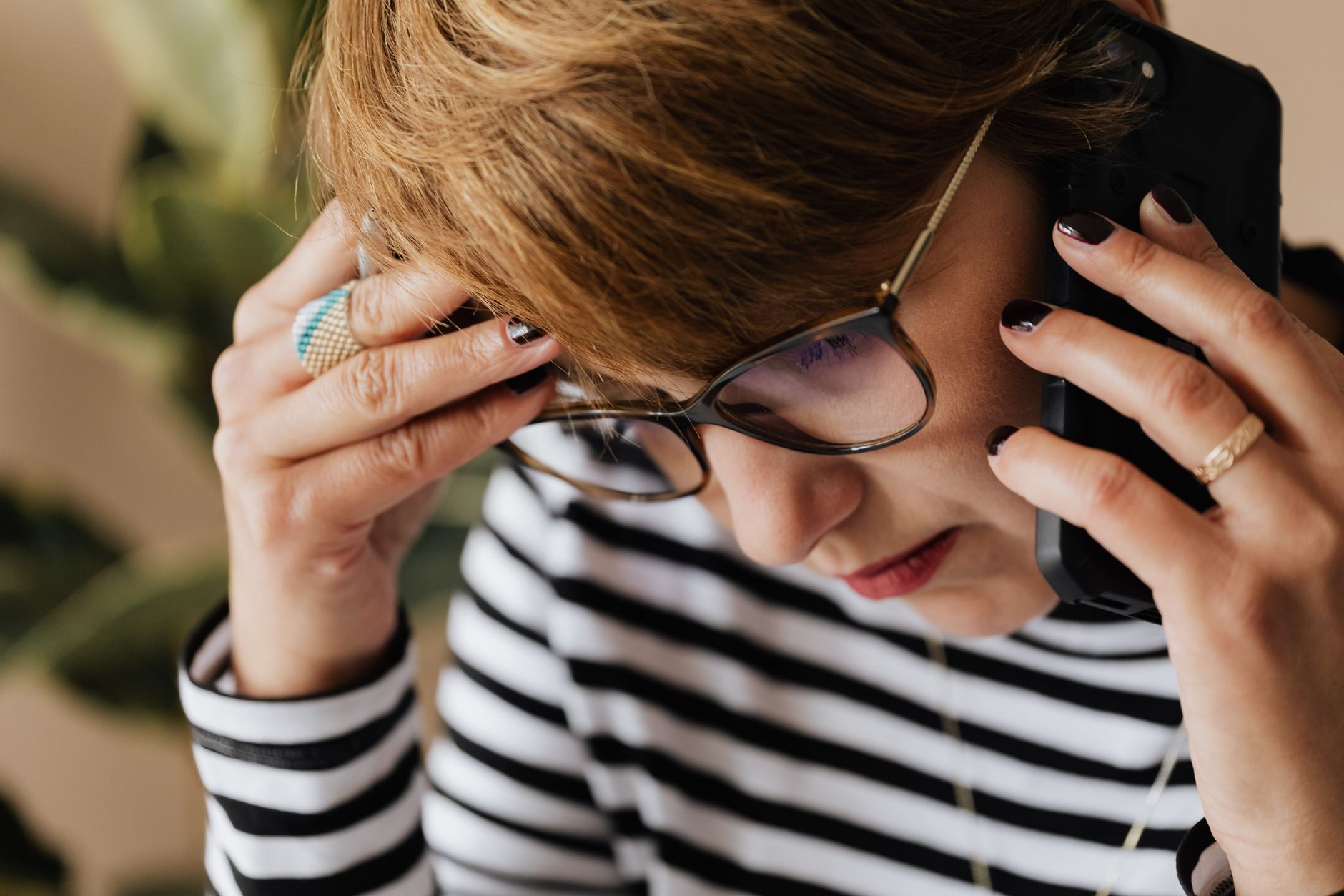 A concerned person sits at a kitchen table with a laptop and phone, calling their bank to report fraudulent activity.